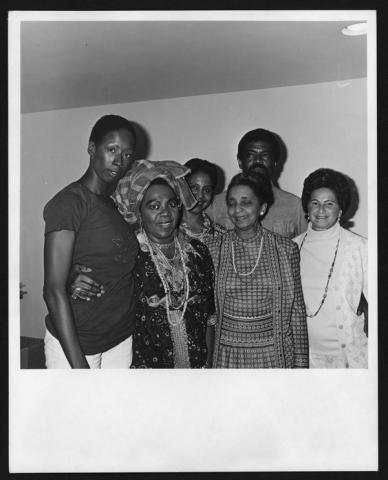 A black-and-white photo featuring Judith Jamison, Pearl Primus, Alvin Ailey, and three other guests. They are standing together in a group, smiling, with Primus dressed in elaborate traditional attire and the others in casual or formal clothing.
