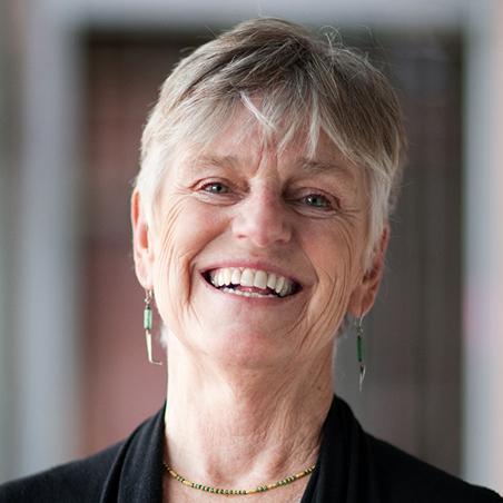 A white haired woman smiling in her headshot. She is wearing a black blazer and a necklace and earrings.