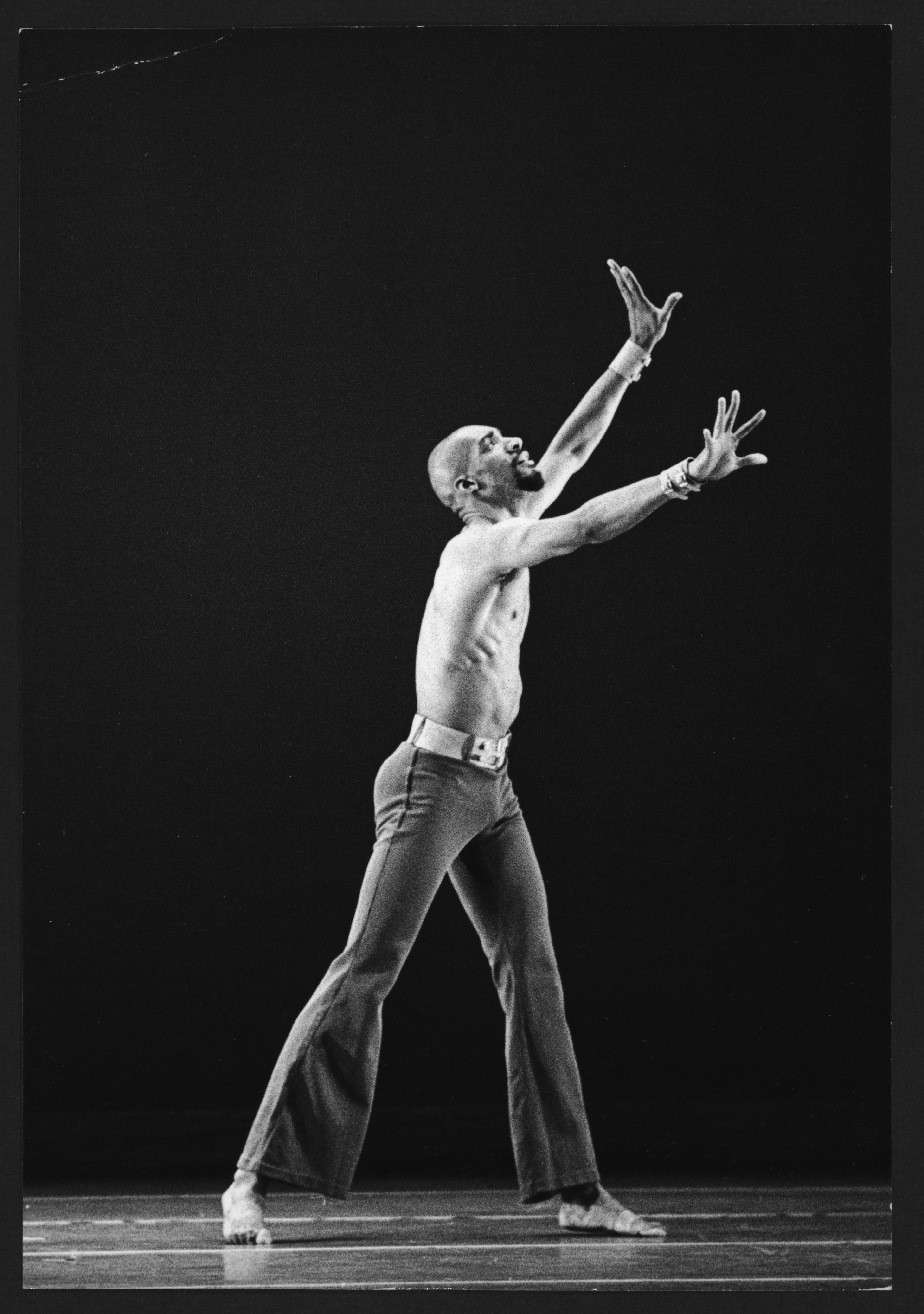 A man looks right on stage. His arms are in a V at a 45 degree angle and his legs are apart.