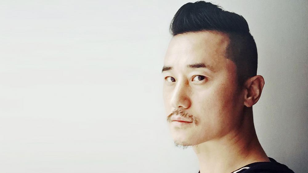 A man's headshot on a white background. He has a light mustache.