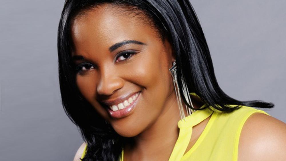 A black woman smiles for the camera. She is wearing a yellow shirt.