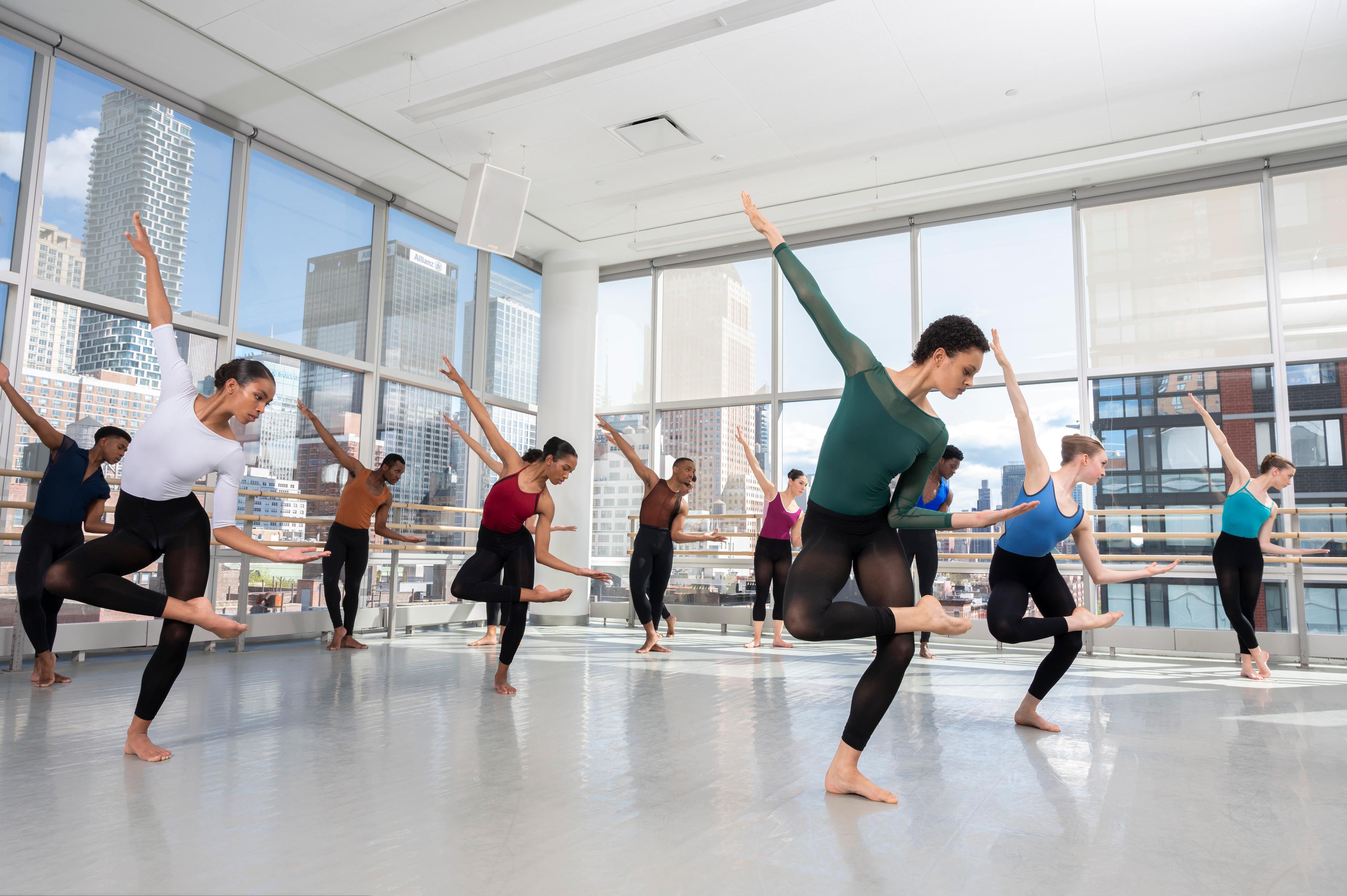 A classroom of dancer students with one leg in posse, one arm in the air, and the other close to their body