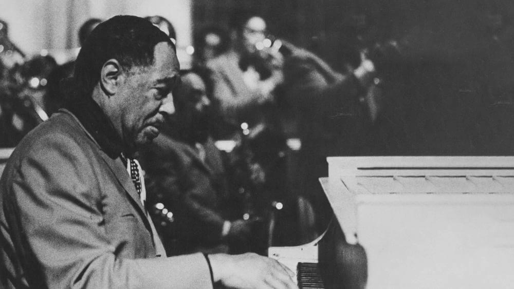 A black and white photo of Duke Ellington playing piano.