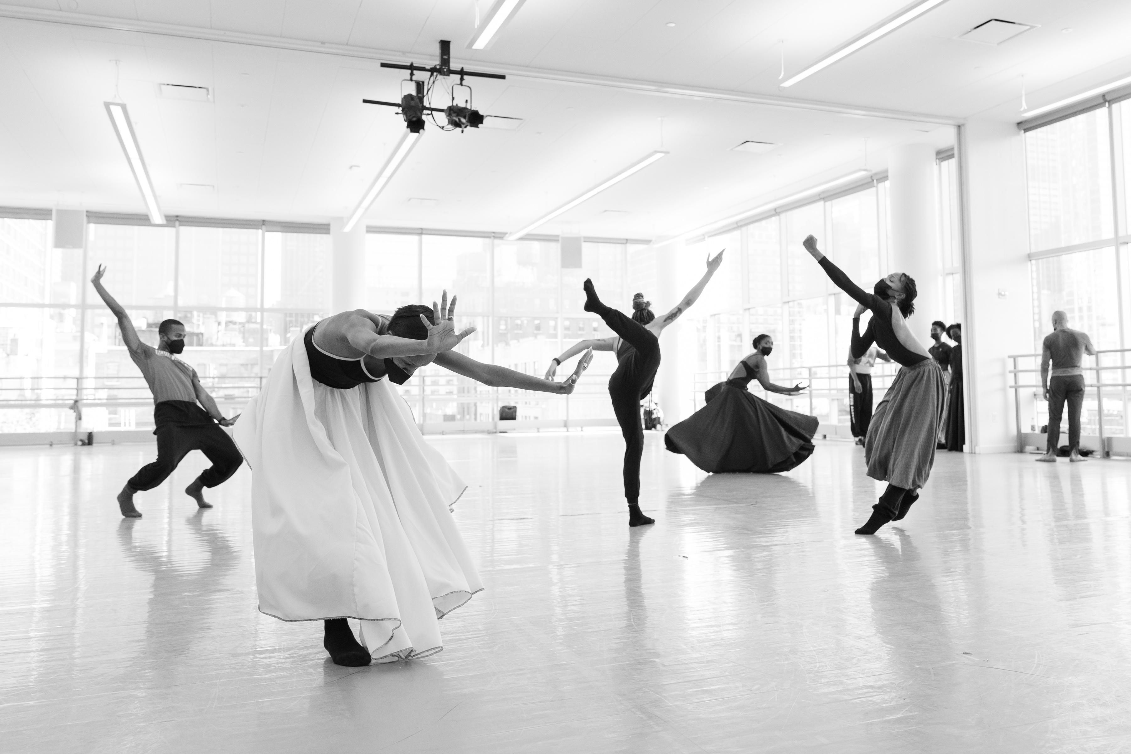 The black-and-white image captures a poignant moment during a rehearsal of Alvin Ailey's "Survivors" by the Alvin Ailey American Dance Theater. The dancers are positioned in expressive, upward-reaching postures, conveying a sense of struggle and determination. Their movements create strong, dynamic lines, emphasizing the emotional depth of the piece. The studio's expansive windows flood the room with natural light, illuminating the dancers and highlighting their powerful physicality.