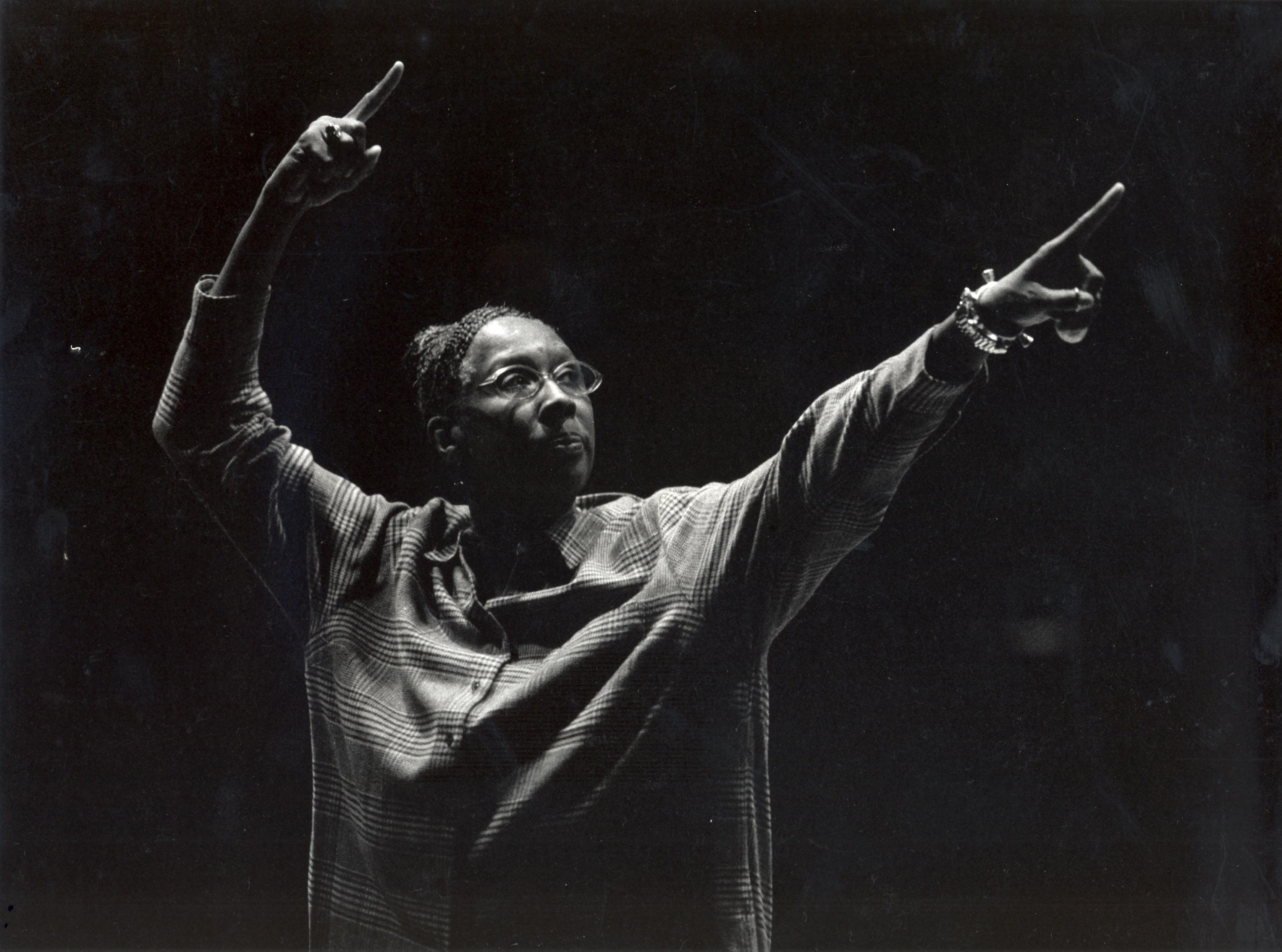 A black and white archival image of Judith Jamison striking a pose pointing high with both hands and looking into the distance