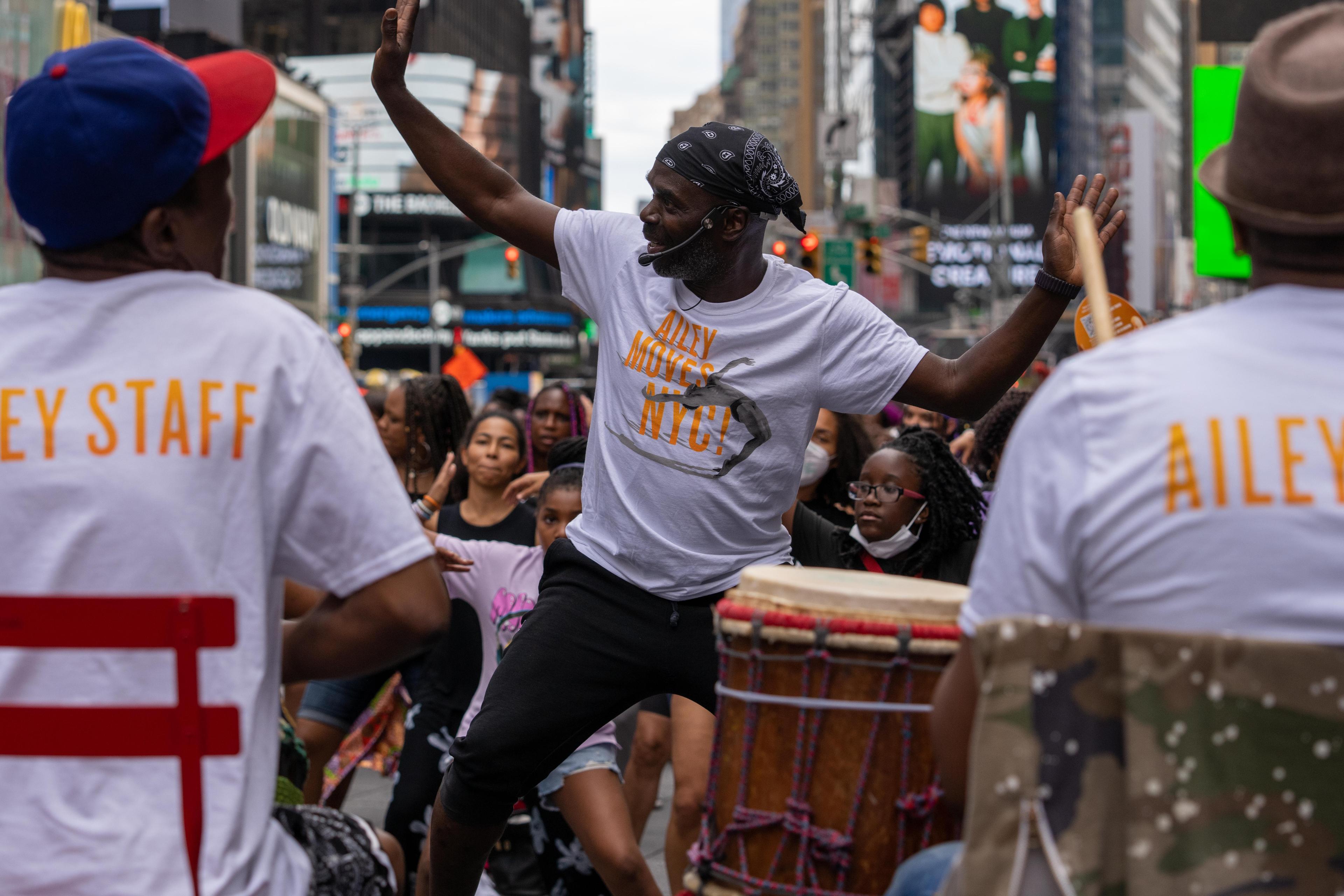 Instructor Maguette Camara in Times Square leading a crowd of participants; two drummers are in the foreground