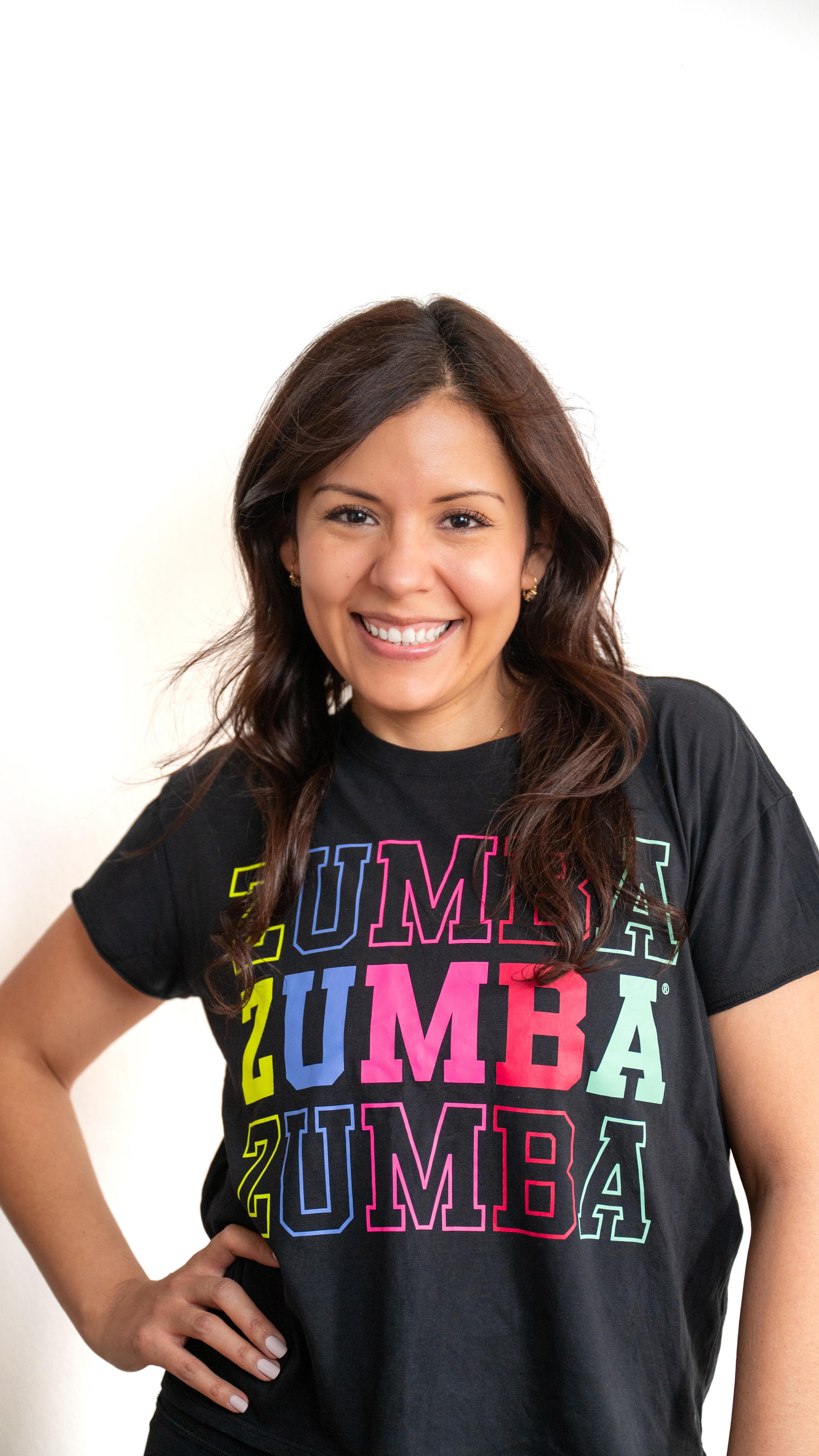 A woman with long dark hair smiling wearing a black Zumba t-shirt with colorful text