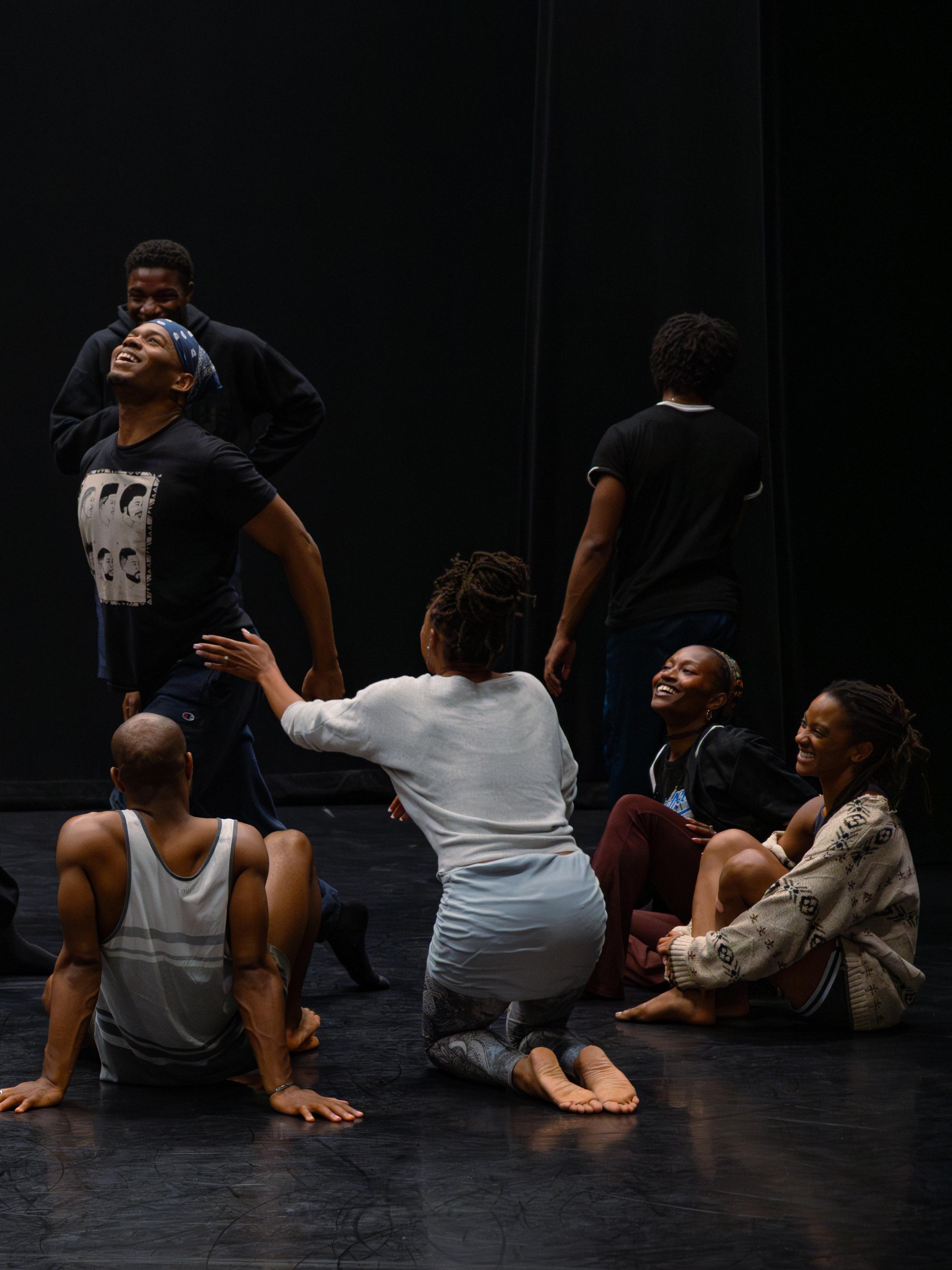 Samantha Figgins directing the cast of The Holy Blues in the studio. The dancers are seated in a circle on the floor while one dancer performs with their chest pointed to the ceiling.