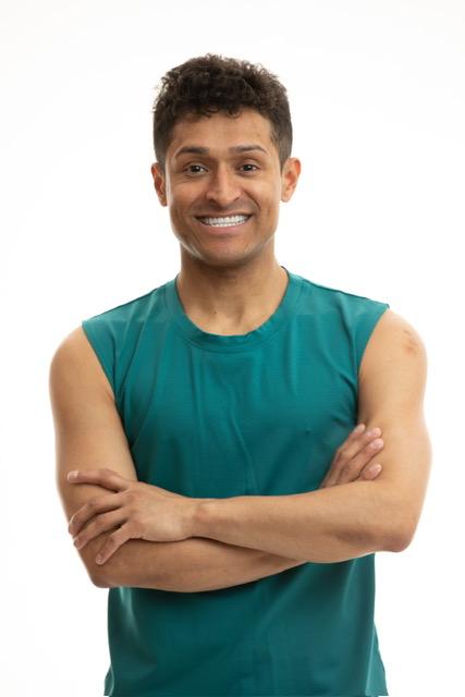 Zumba instructor Wilson Gutierrez in a teal blue tank top, smiling with his arms crossed