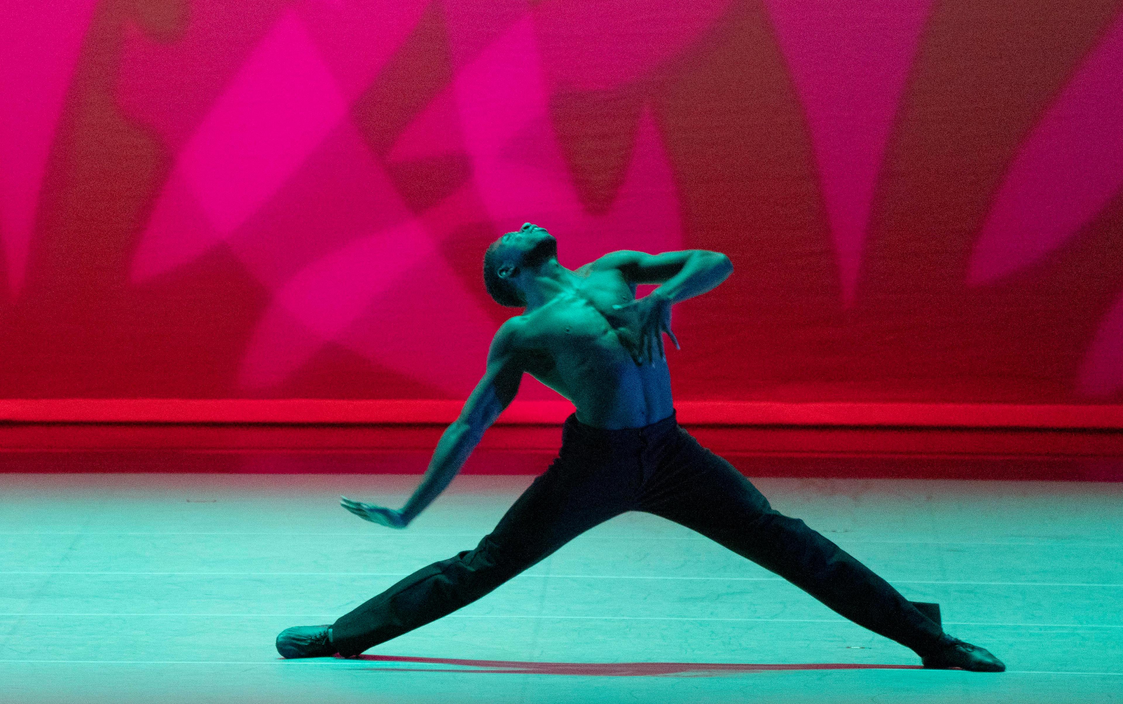 An Ailey dancer in a wide leg stance, leaning their upper body backward