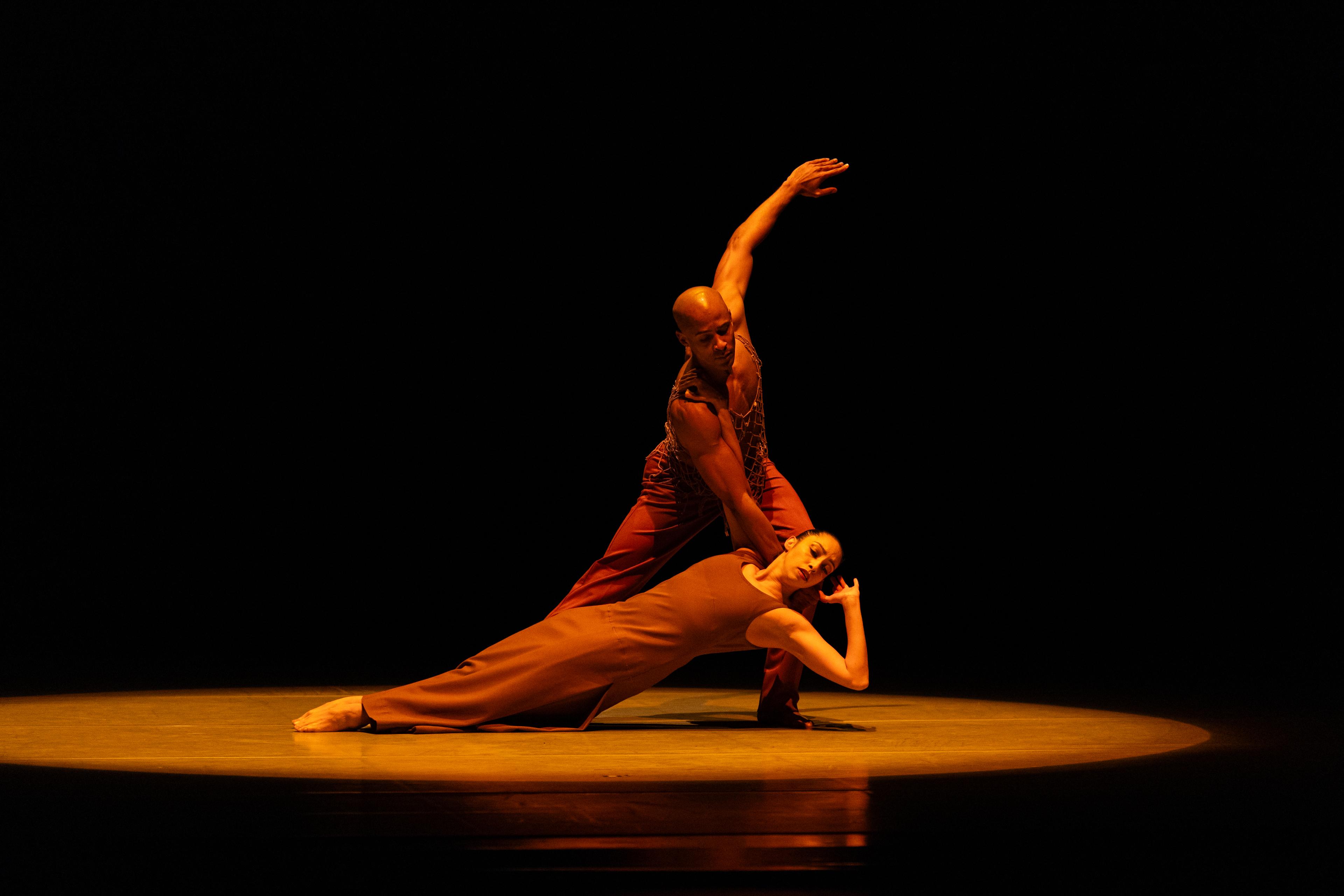 Two dancers from Alvin Ailey American Dance Theater, one very close to the ground laying flat with the other holding them by the neck