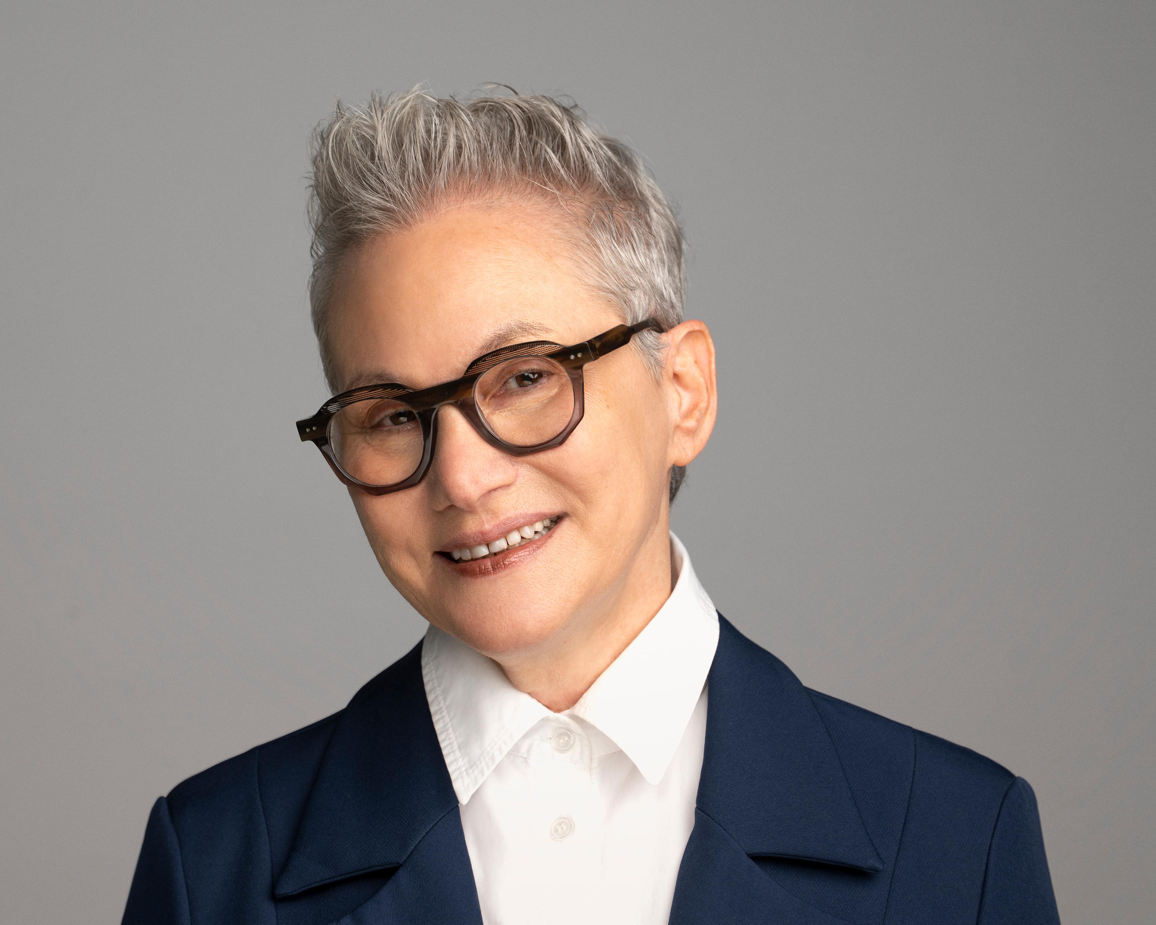 A headshot of Heidi Miller, a white woman with short grey hair, wearing glasses, a white shirt, and black blazer