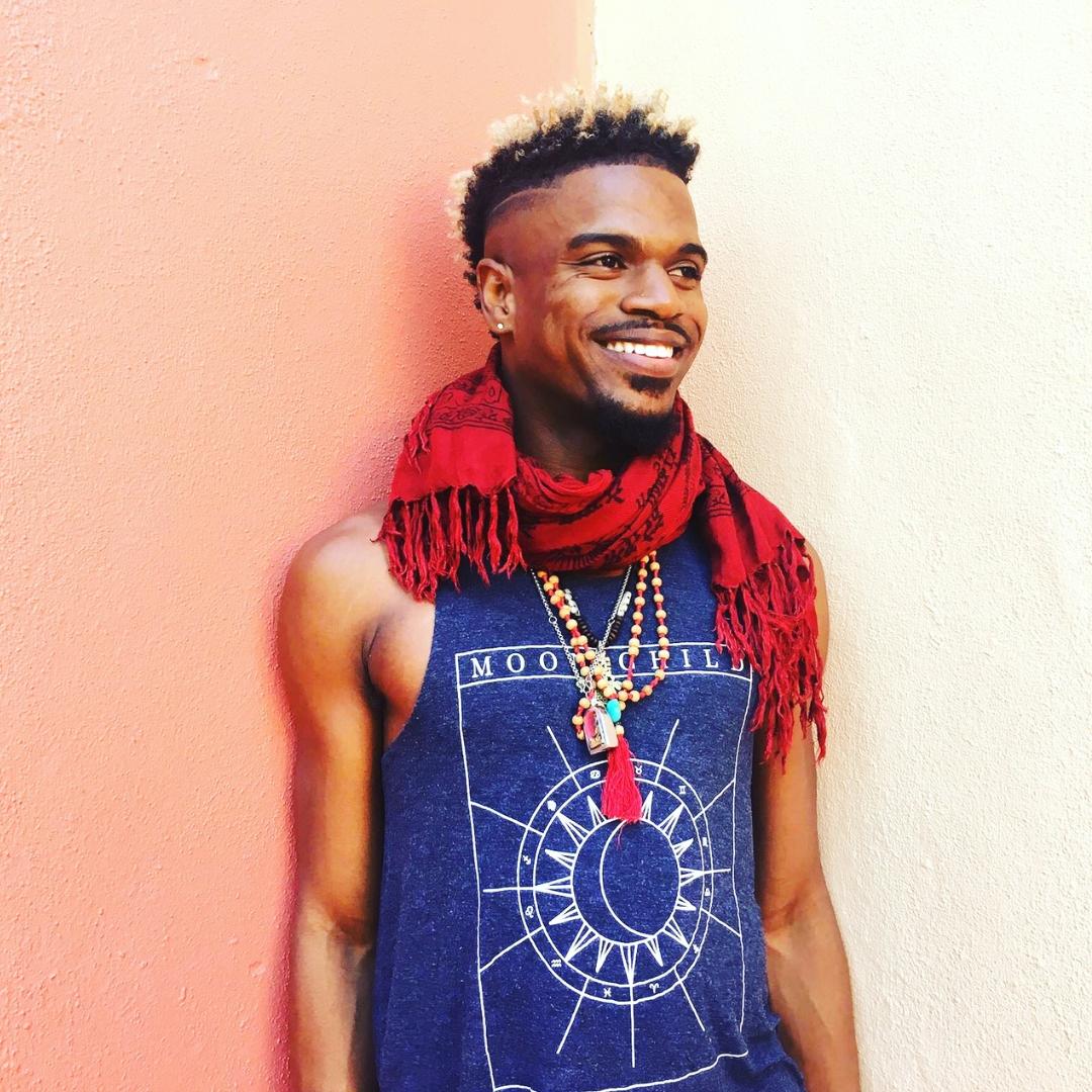Mychal A. Bryan wearing a blue tank top with a moon graphic and a bright red scarf and necklaces