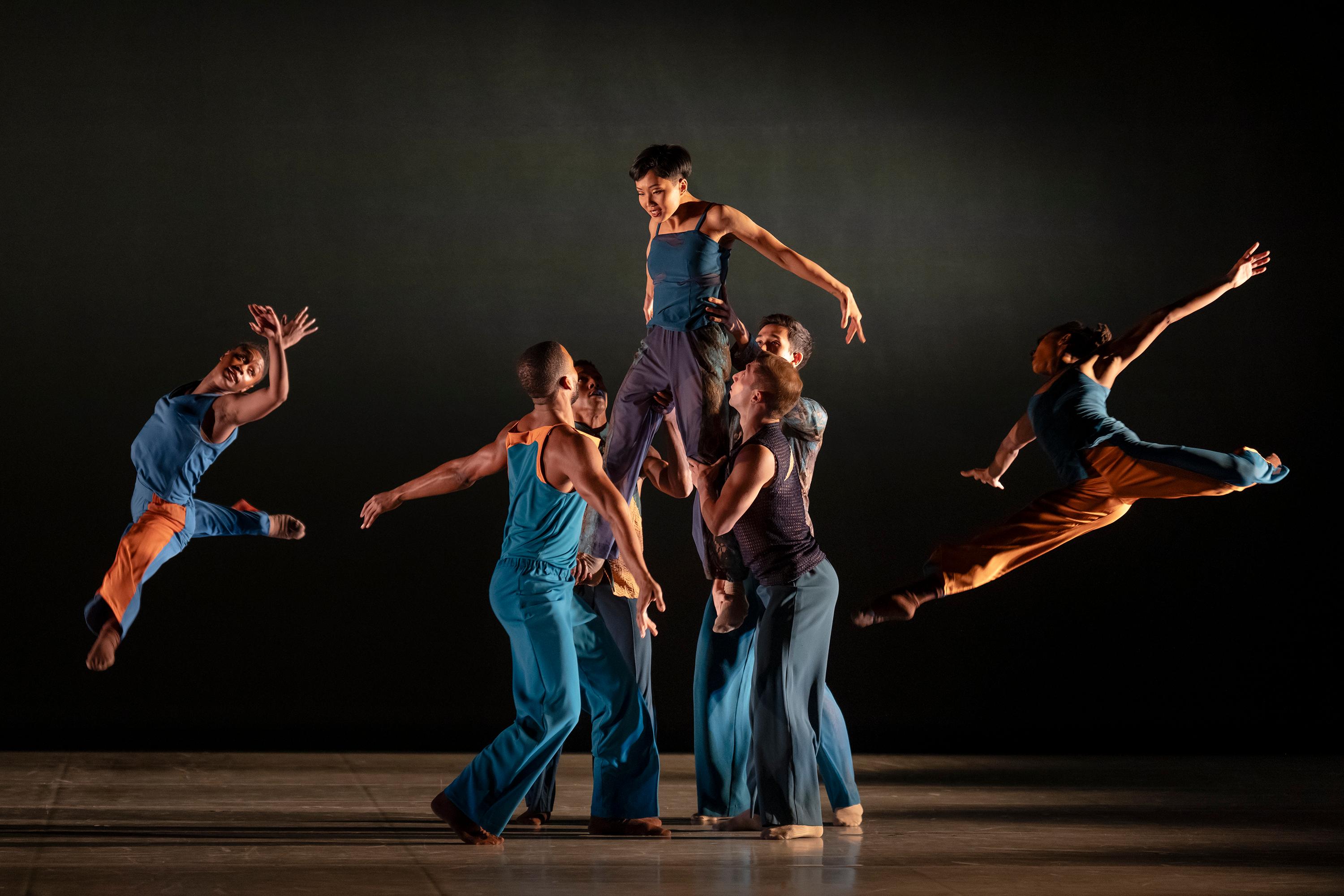 A group of dancers with 1 standing on their knees and 2 dancers jumping on the sides