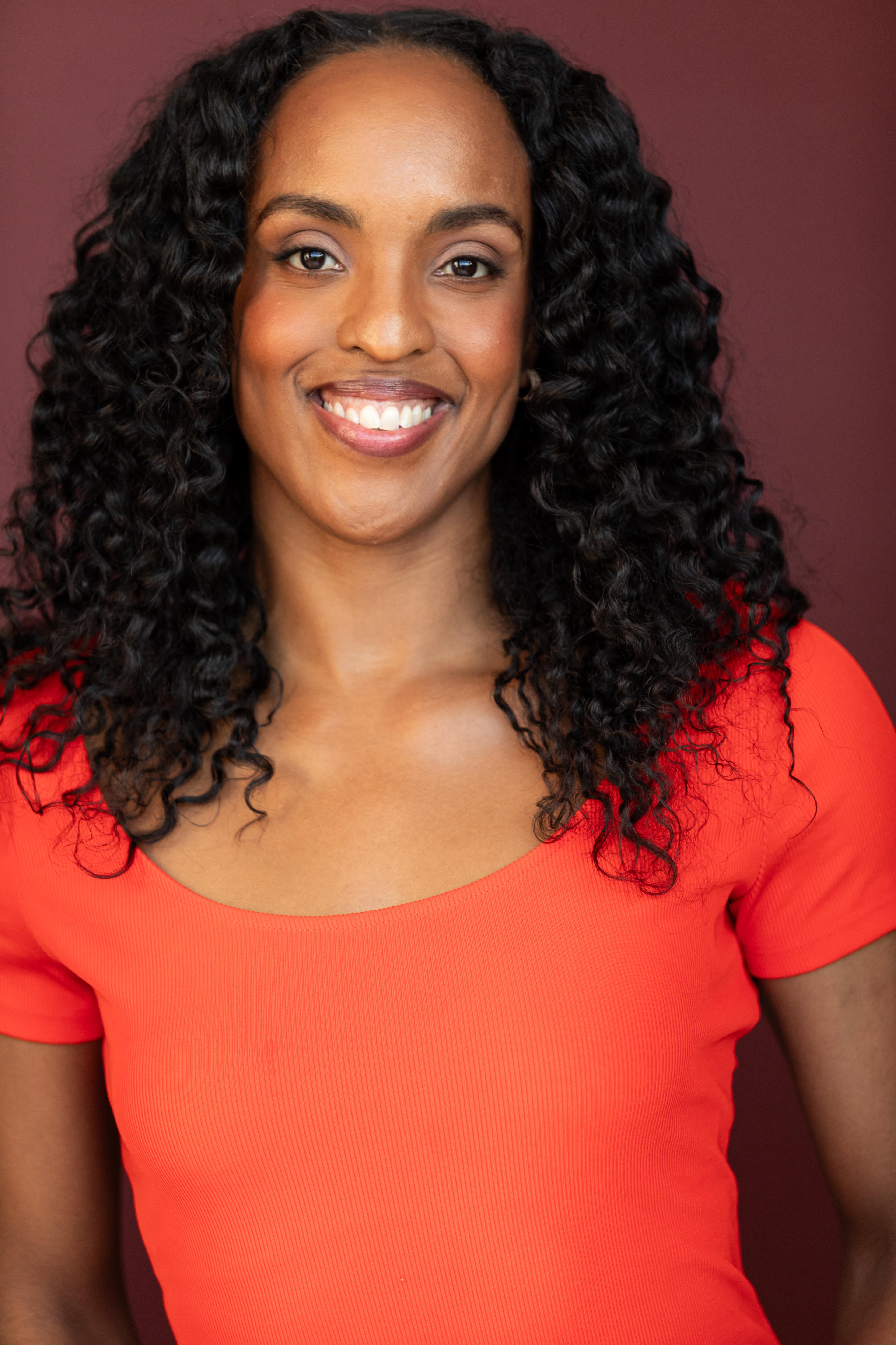 Janine Beckles smiling wearing a red-orange shirt
