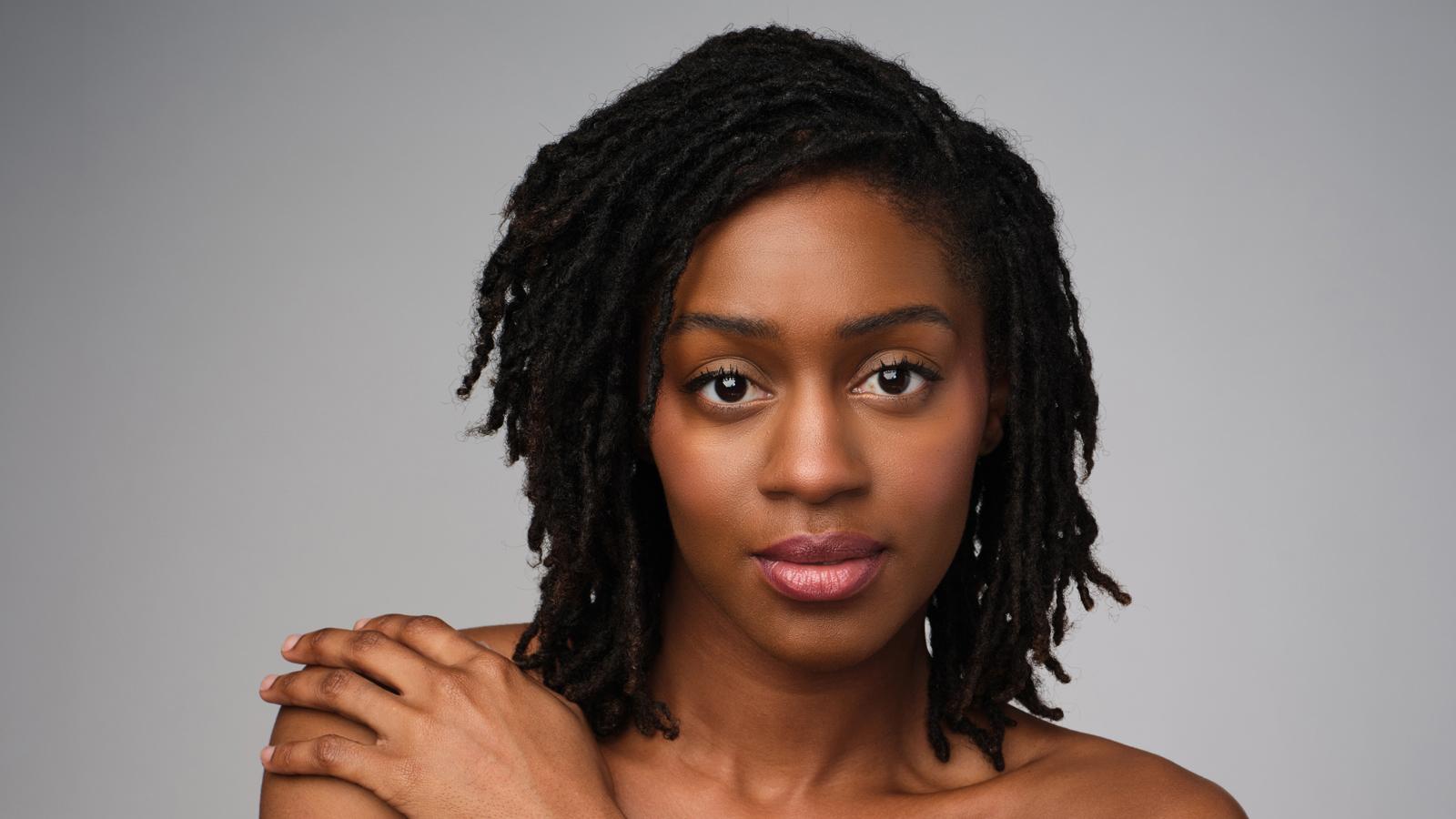 A headshot of Corrin Rachelle Mitchell, a black female dancer with shoulder-length braided hair