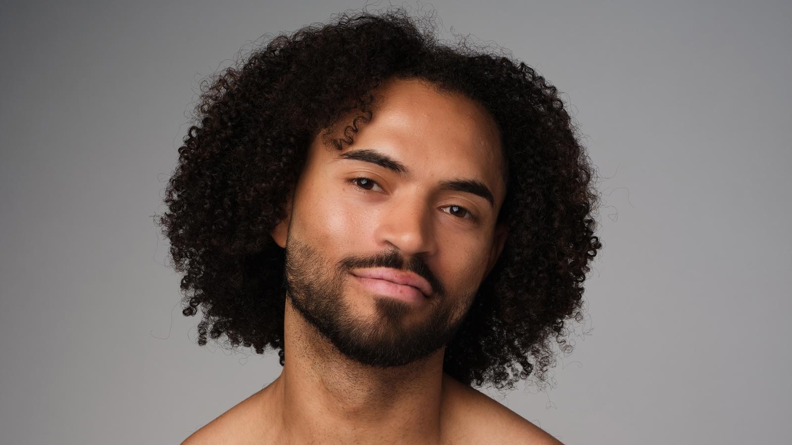 A headshot of James Gilmer, with just above shoulder length dark curly hair and facial hair