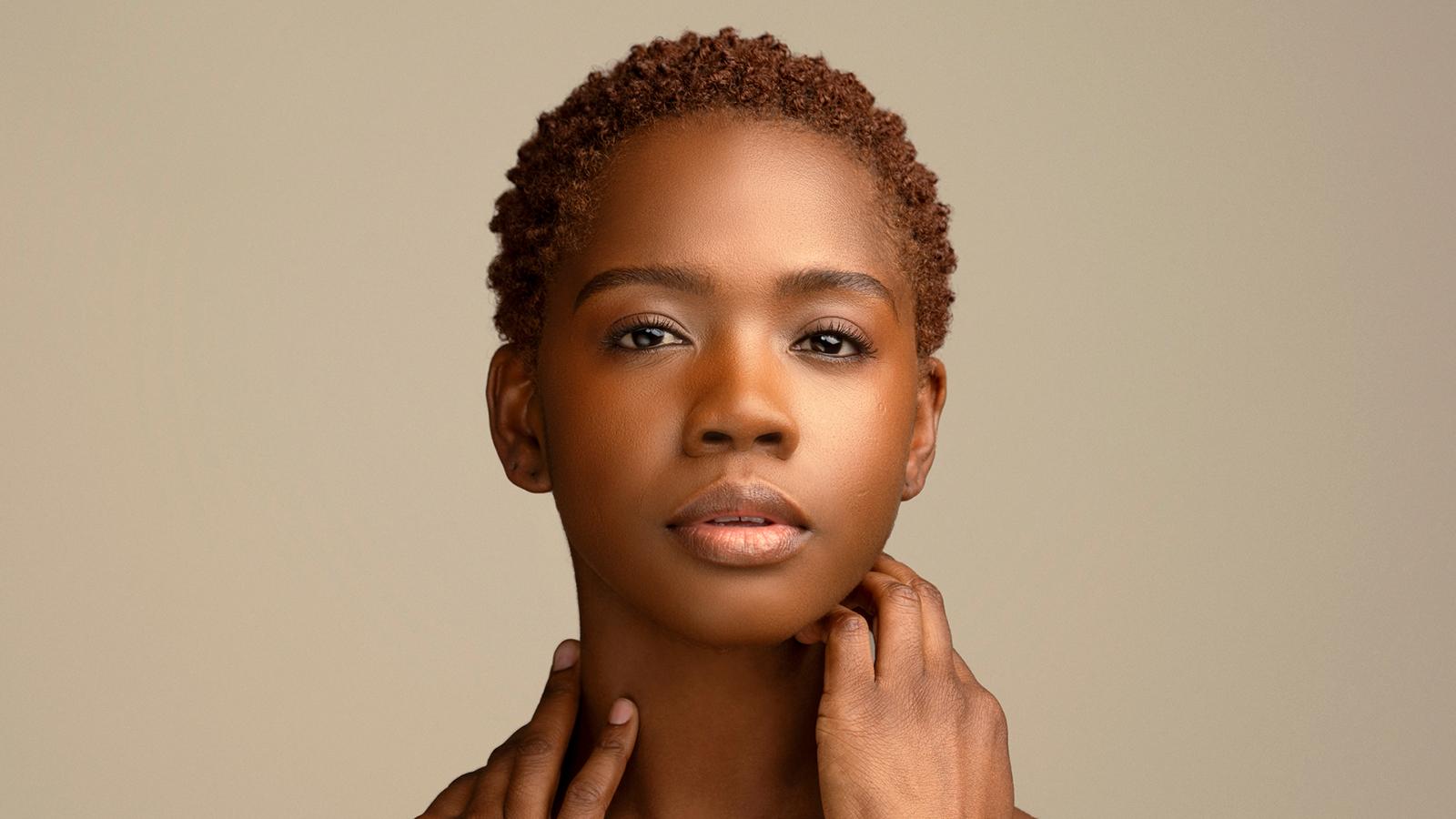 A headshot of Jessica Amber Pinkett, a female dancer with very short brown hair with her hands touching her neck