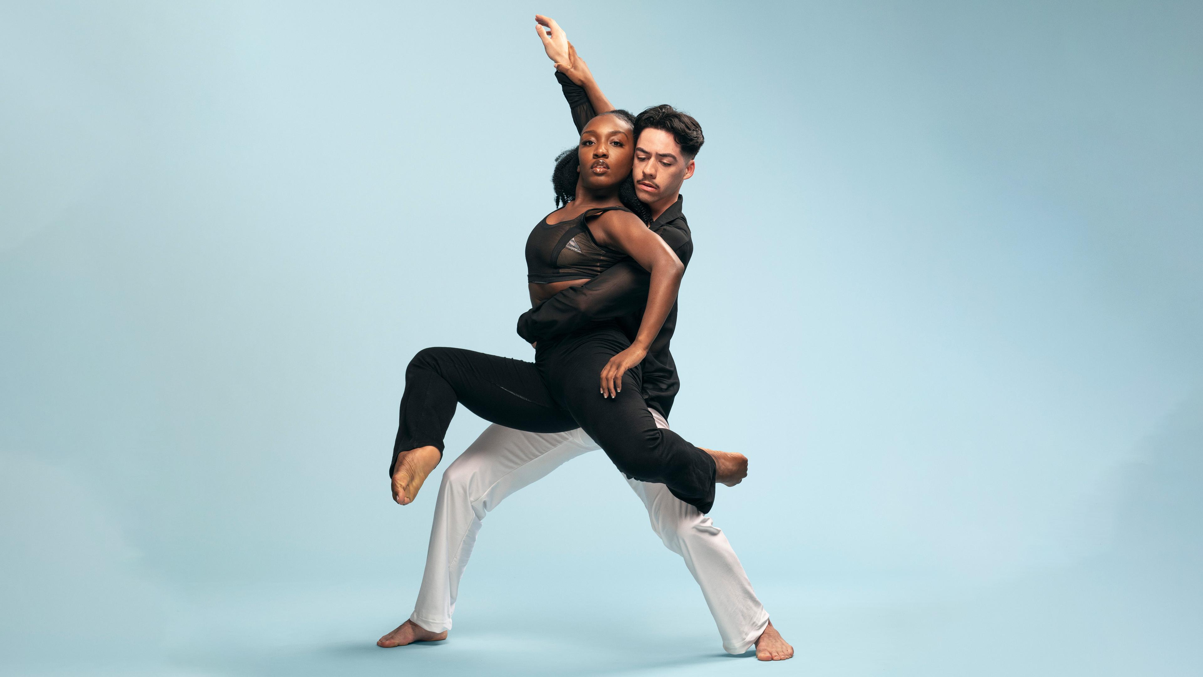 Male dancer lifting female dancer in front of blue background