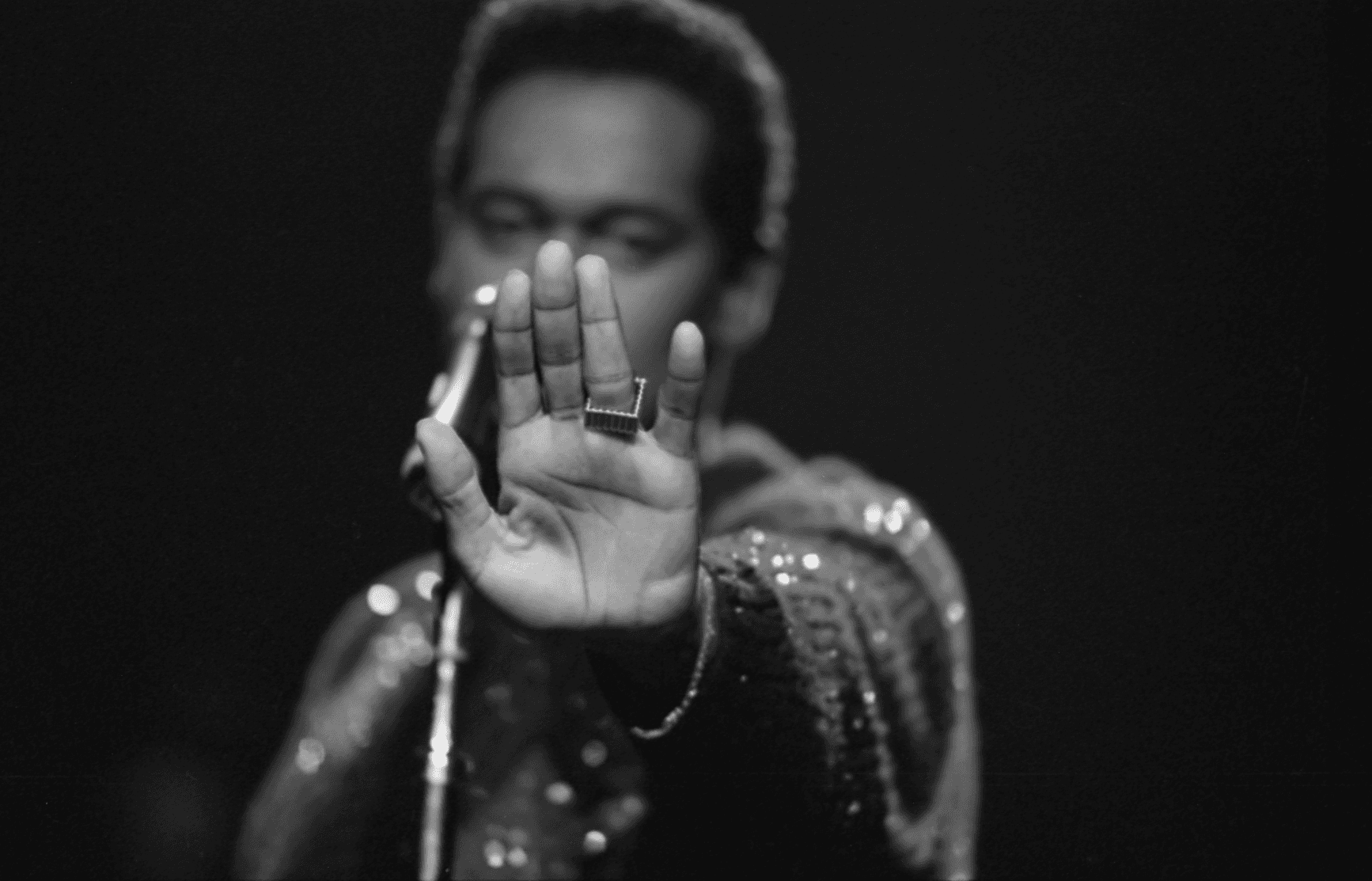 Black and white photo of Luther Vandross holding his hand out to the camera palm first, as if to shield his face