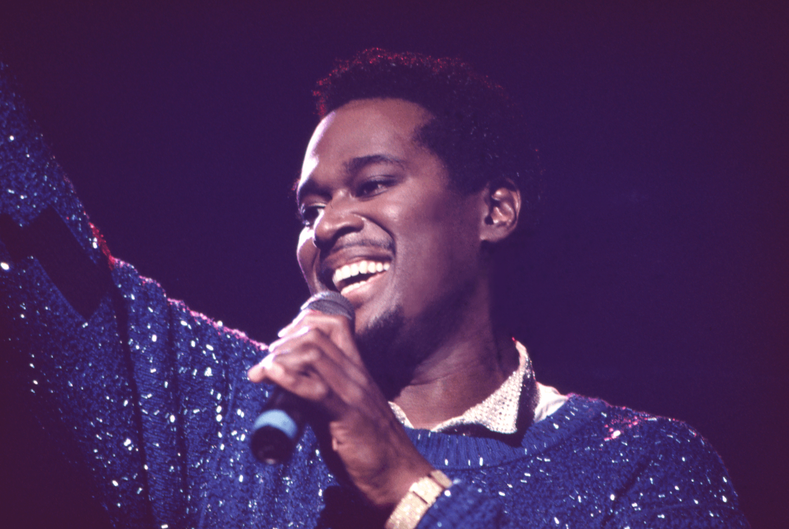 R&B singer Luther Vandross on stage, holding a microphone and smiling