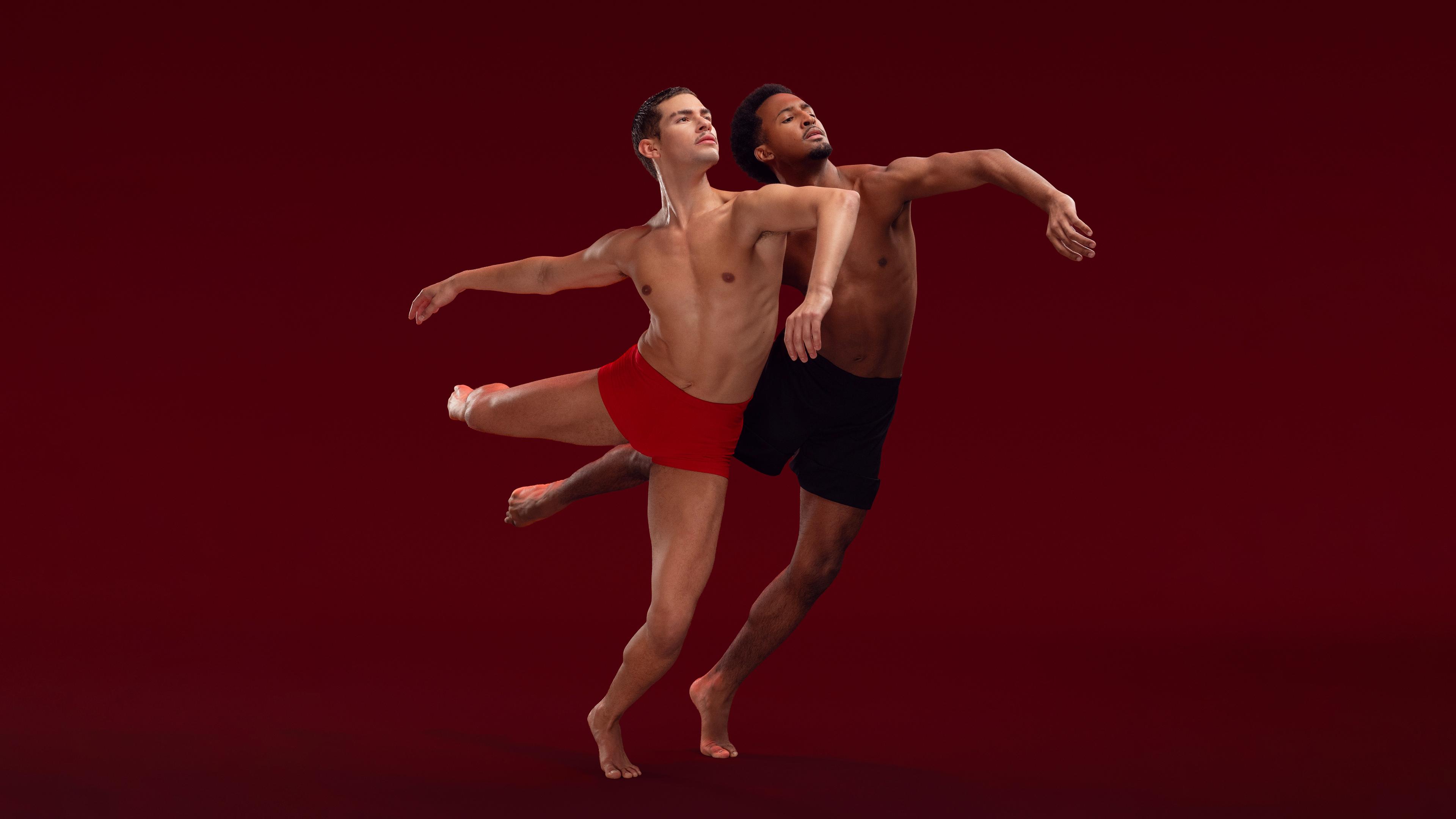 2 male Ailey II dancers in attitude next to each other in front of a red background