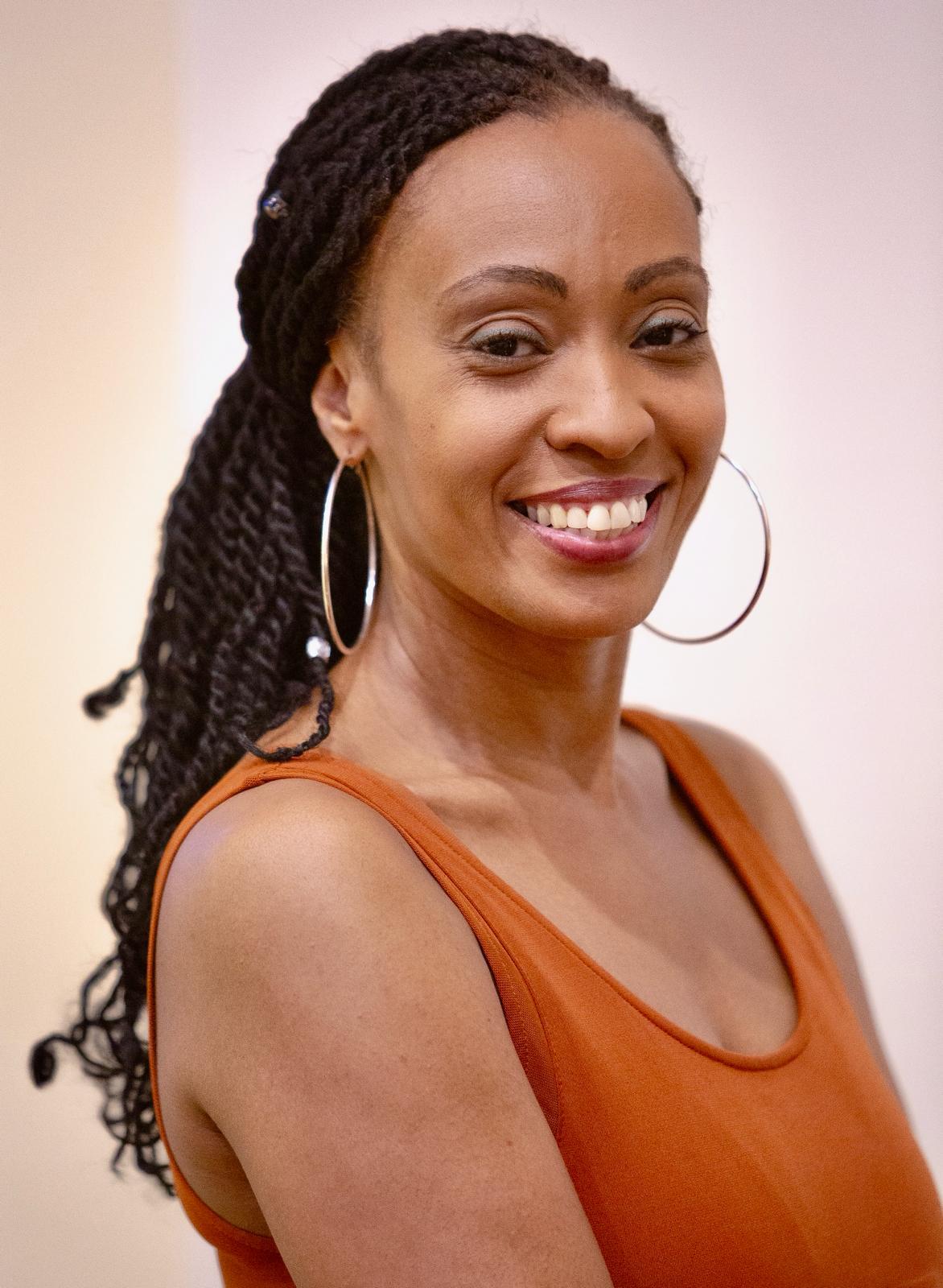 A headshot of Jessica St. Vil, a black woman wearing an orange tank top and large silver hoops