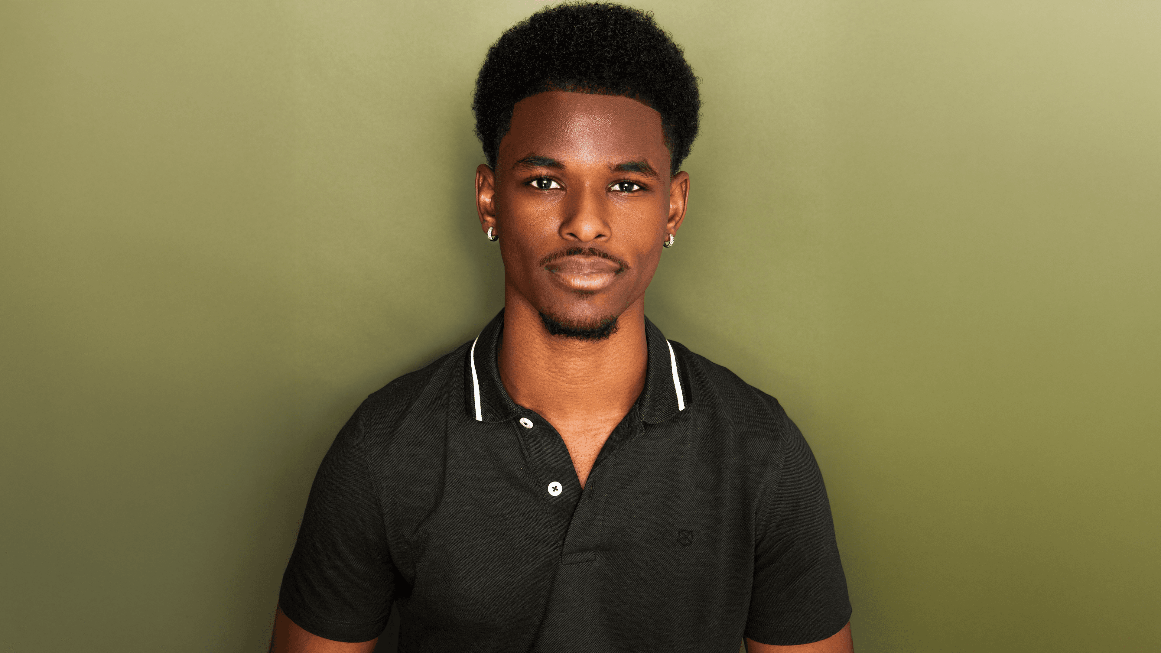 Wesley Wray against a sage green background wearing a black polo