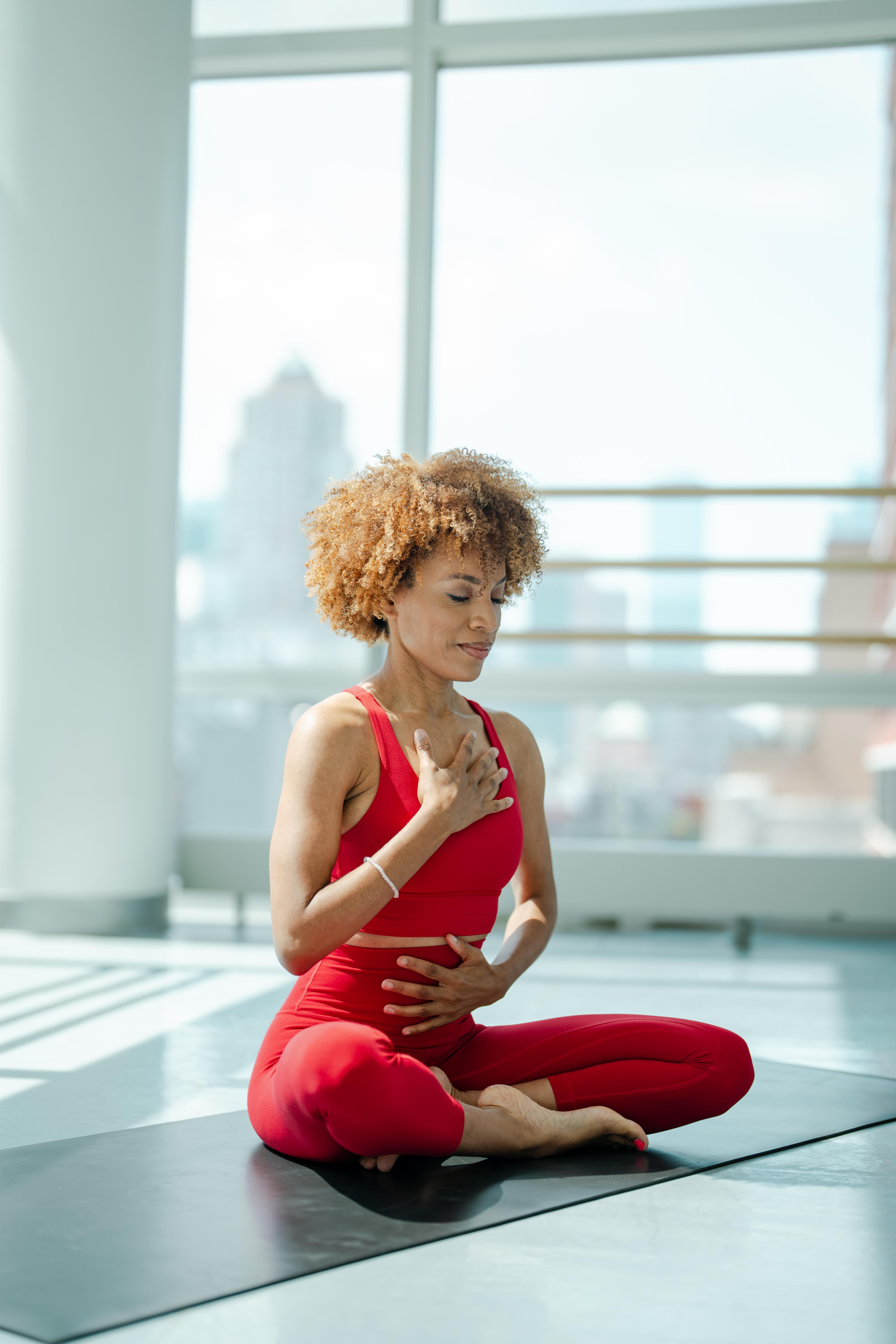 Pilin Anice meditating on a yoga mat at the Ailey Studios wearing a red athletic set