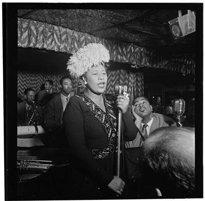 Black and white photo of Ella Fitzgerald singing in a New York club with Dizzy Gillespie sitting by her side